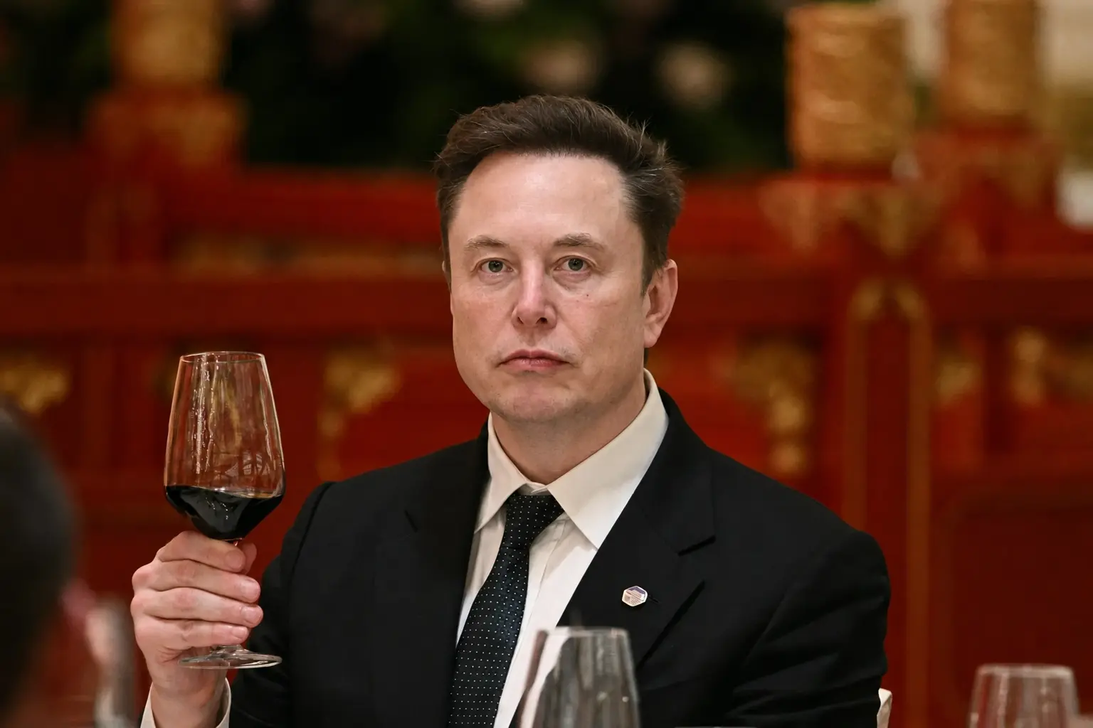 Elon Musk tenant une verre de vin dans un restaurant.