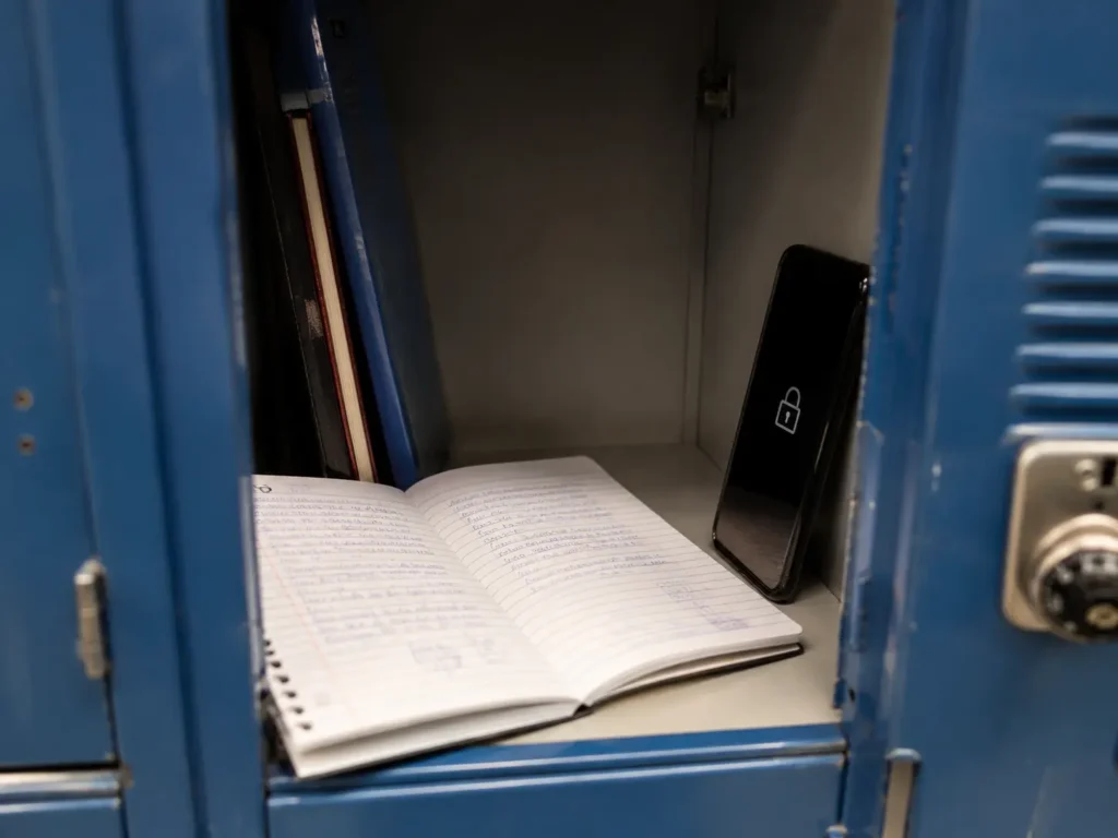 Cahier d'écolier ouvert près d'un téléphone verrouillé dans un casier scolaire