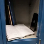 Cahier d'écolier ouvert près d'un téléphone verrouillé dans un casier scolaire