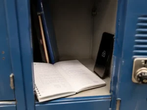 Cahier d'écolier ouvert près d'un téléphone verrouillé dans un casier scolaire