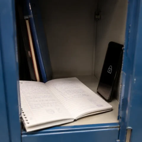 Cahier d'écolier ouvert près d'un téléphone verrouillé dans un casier scolaire