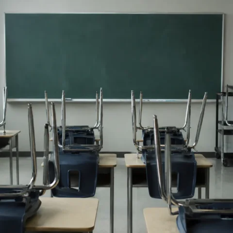 Classe vide, chaises empilées sur les pupitres devant un tableau effacé