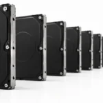 Longue rangée de disques durs noirs identiques alignés sur une surface blanche