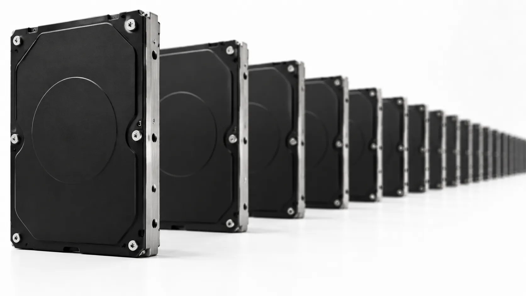 Longue rangée de disques durs noirs identiques alignés sur une surface blanche