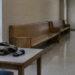 Corridor de palais de justice désert, bancs de bois vides devant une porte de salle d'audience fermée.