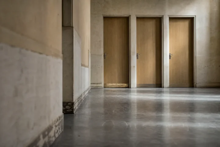 Trois portes identiques et closes au bout d'un couloir, seuils inégalement usés
