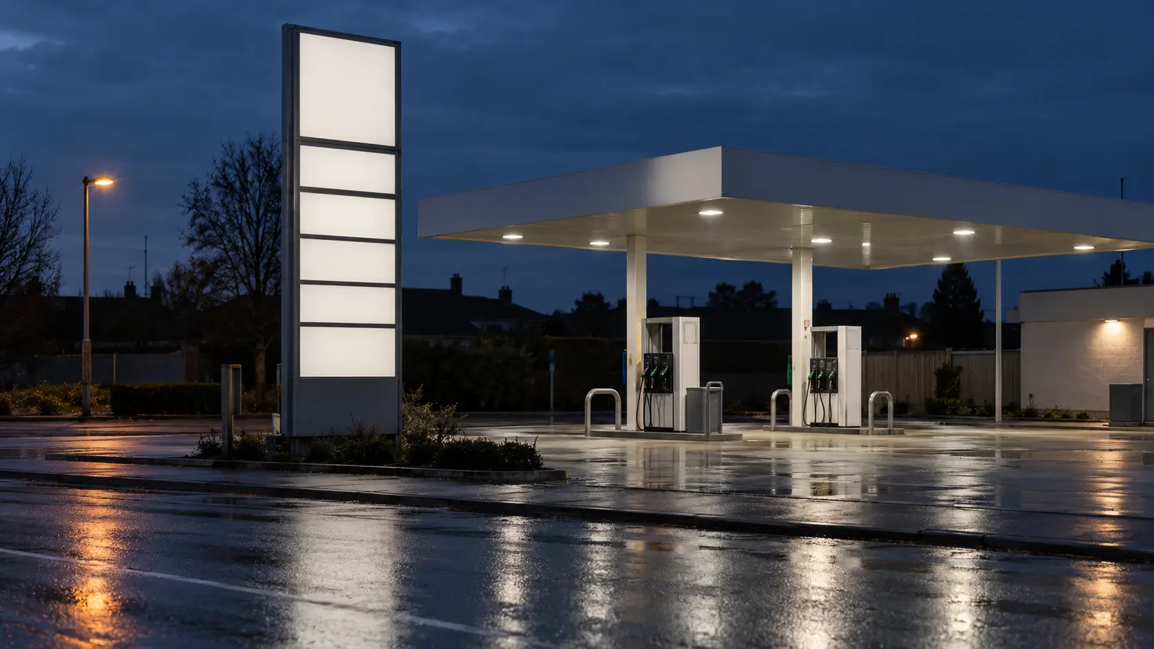 Totem de prix d'une station-service au crépuscule, panneaux d'affichage entièrement vides au-dessus d'une chaussée mouillée.