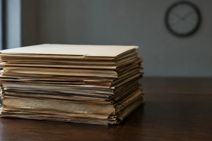 Pile de chemises judiciaires jaunies surmontée d'une chemise neuve sur une table sombre