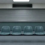 Salle d'attente déserte d'un bureau d'immigration : chaises vides devant un guichet fermé par un rideau métallique.