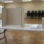 Salle communautaire vide aménagée en bureau de vote, isoloir de carton et urne fermée
