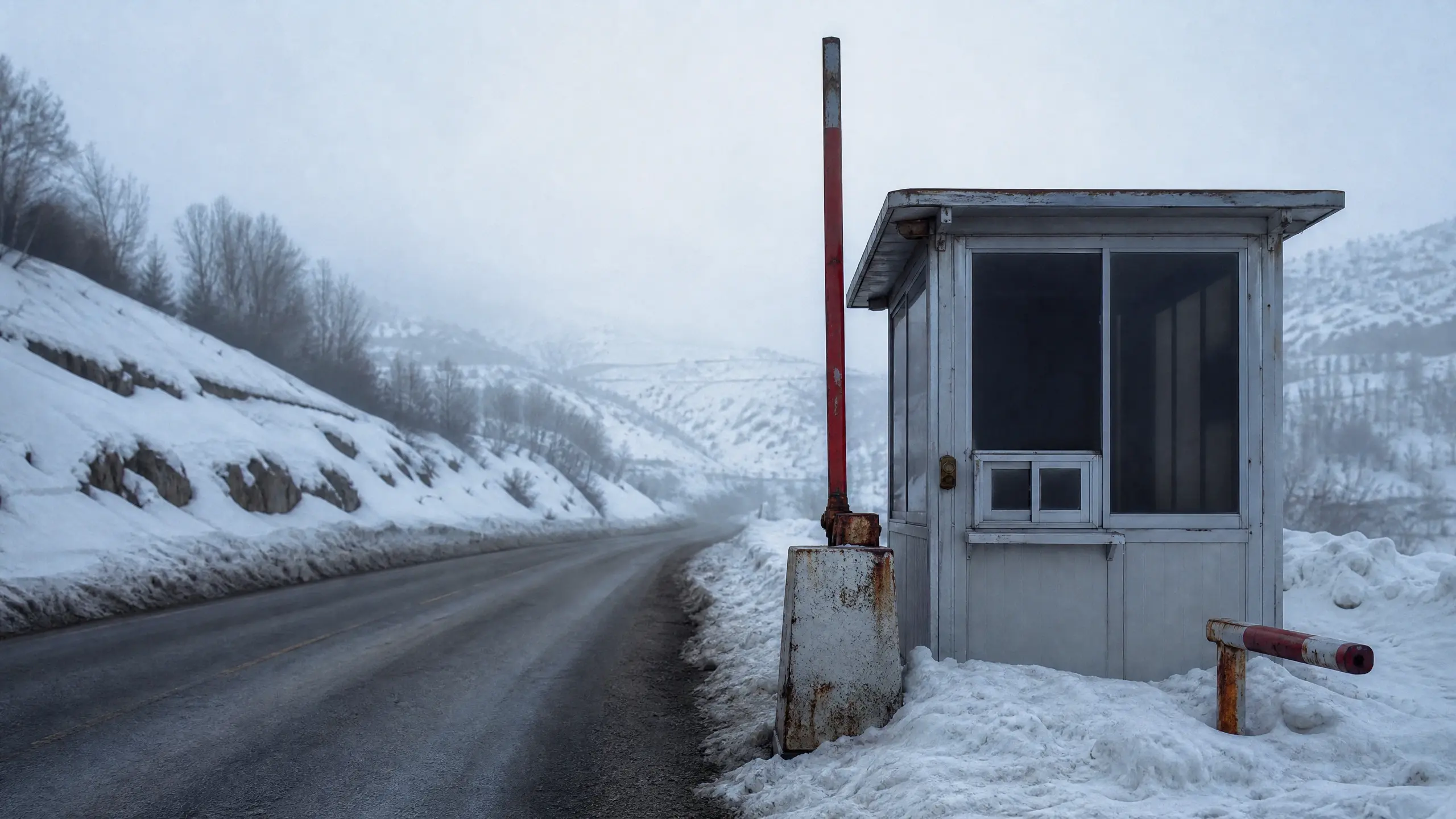 Poste frontalier de montagne, barrière levée, guérite vide, route déneigée sous la neige