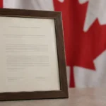 Certificat de citoyenneté canadienne encadré, posé devant un drapeau canadien flou en arrière-plan.