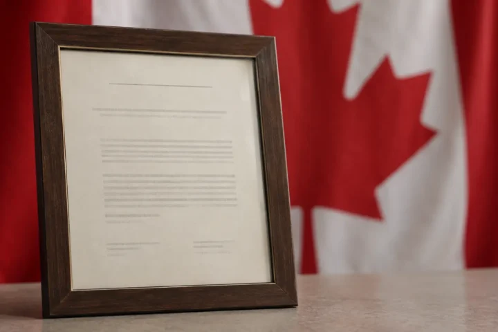 Certificat de citoyenneté canadienne encadré, posé devant un drapeau canadien flou en arrière-plan.