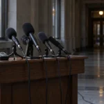 Micros de journalistes posés sur un lutrin vide dans un couloir sombre