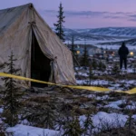 Tente de toile isolée parmi des épinettes enneigées au crépuscule, ruban de sécurité et policier flou au loin
